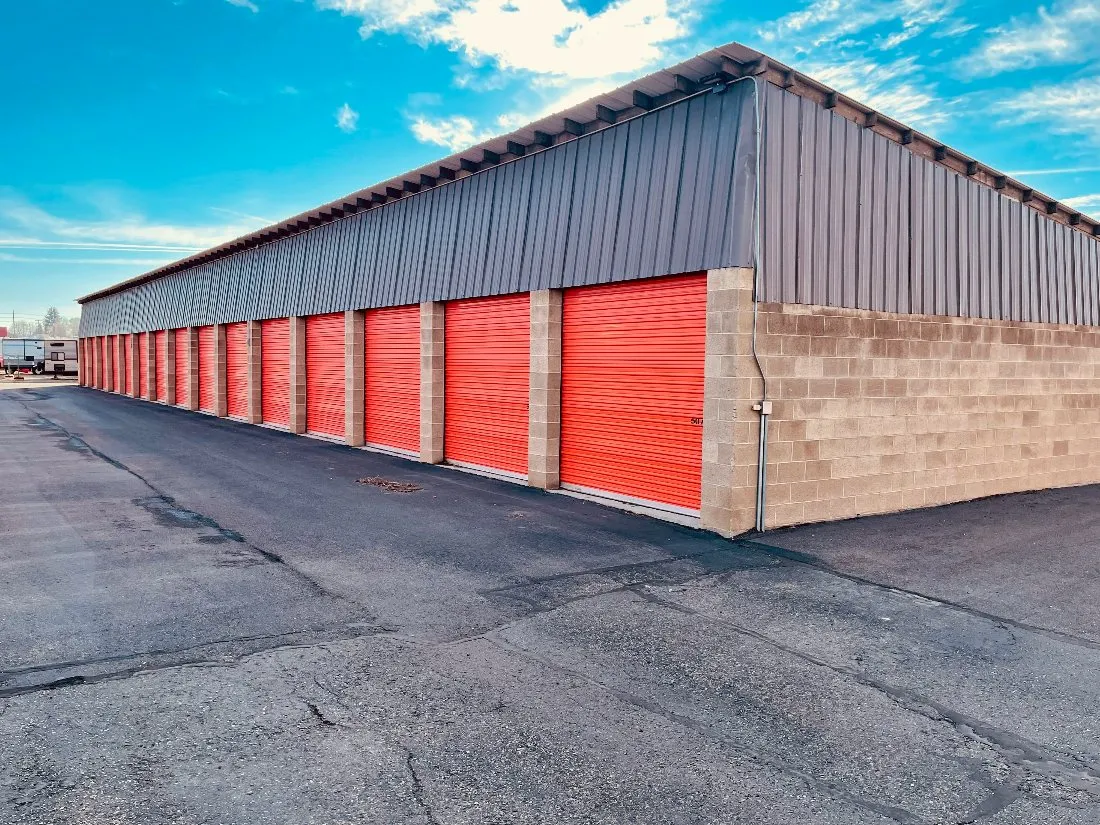 Drive-up storage building with orange roll-up doors and a wide paved drive aisle